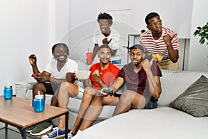 Young african group of friends sitting on the sofa at home playing video games pointing thumb up to the side smiling happy with