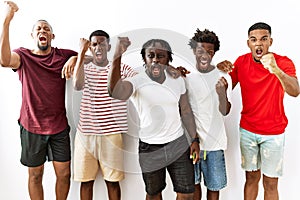 Young african group of friends standing together over isolated background angry and mad raising fist frustrated and furious while