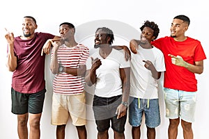 Young african group of friends standing together over isolated background smiling with happy face looking and pointing to the side