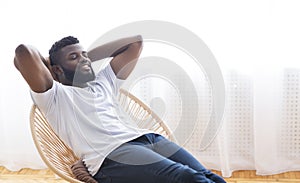 Young african guy relaxing at home, resting on chair