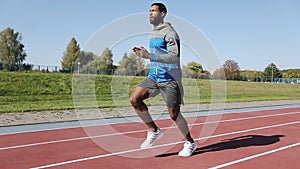 Young African male athlete sprinting alone down a running track on a sunny day.