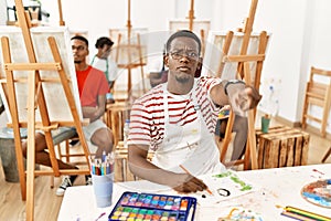 Young african man at art studio pointing with finger to the camera and to you, confident gesture looking serious