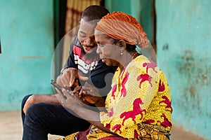 a young african man assisting an elderly woman using her phone