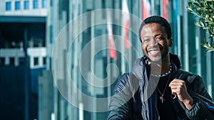 Young African man in a black outfit walking in a street posing in front of a glass paneled building