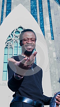 Young African man in a black outfit walking in a street posing in front of a glass paneled building