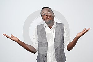 Young african man in blue shirt being at a loss, showing helpless gesture with arm and hand