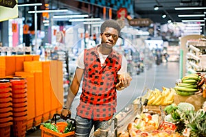 Young african man buying vegetables and fruits in grocery section at supermarket. Black man choose vegetables and fruits