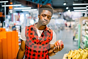 Young african man buying vegetables and fruits in grocery section at supermarket. Black man choose vegetables and fruits