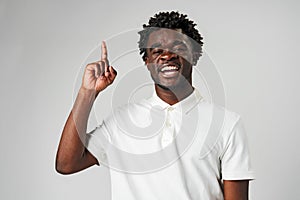 Young African Man in Casual Attire Pointing Upwards With a Smile Against a Grey Background