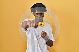Young african man with dreadlocks standing over yellow background punching fist to fight, aggressive and angry attack, threat and