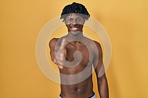 Young african man with dreadlocks standing shirtless smiling friendly offering handshake as greeting and welcoming