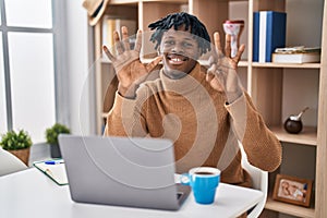 Young african man with dreadlocks working using computer laptop showing and pointing up with fingers number eight while smiling