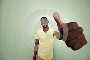 Young african man gesturing thumbs up sign by green wall