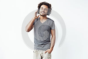 Young african man in headphones listening to upbeat music over white background.