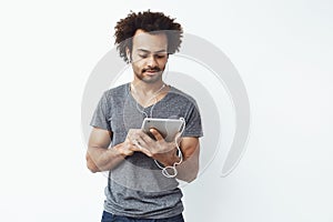 Young african man in headphones looking at tablet over white background.