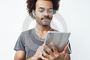 Young african man in headphones looking at tablet over white background.