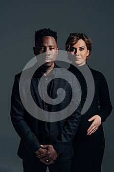 Young african man and his caucasian pregnant woman stand against grey background