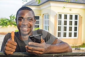 young african man holding his mobile phone smiling and giving a thumbs up