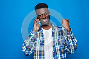 Young african man holding a phone cheering carefree and excited isolated on blue background