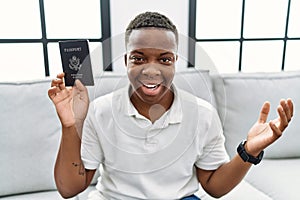 Young african man holding united states passport celebrating victory with happy smile and winner expression with raised hands
