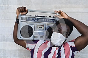 Young African man holding vintage boombox having fun outdoor - Black man wearing face mask while listening music with stereo