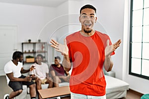 Young african man at home with friends sitting on the sofa at home celebrating victory with happy smile and winner expression with