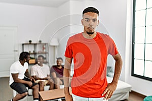 Young african man at home with friends sitting on the sofa at home with serious expression on face