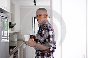 Young african man in the kitchen with mobile phone and coffee