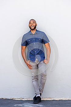 Young african man laughing and leaning against gray wall