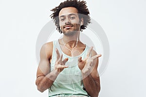 Young african man listening to music in headphones dancing over white background.