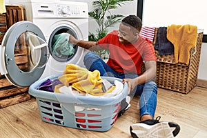 Young african man putting dirty clothes into washing machine at laundry room