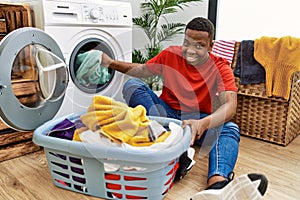 Young african man putting dirty clothes into washing machine at laundry room