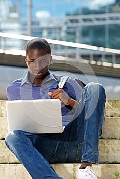 Young african man sitting outdoors and using laptop