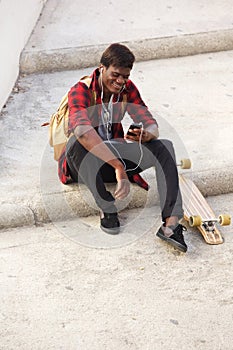 Young african man sitting outside on steps and listening to music