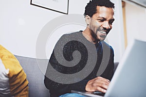 Young African man smiling and using laptop while sitting at his modern coworking place.Concept of happy business people