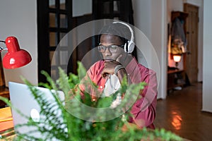 Young African man student wearing headphones watching webinar on laptop while studying online