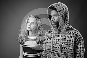 Young African man with teenage girl together against gray background