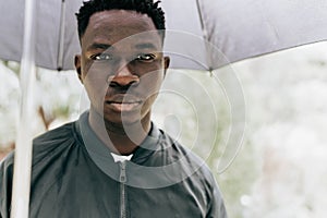 Young African man under black umbrella in rain, sad. Fall or spring weather