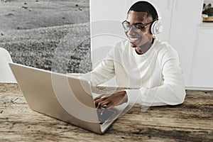 Young african man using laptop computer while wearing headphones at home - Focus on face