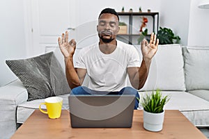 Young african man using laptop at home relax and smiling with eyes closed doing meditation gesture with fingers