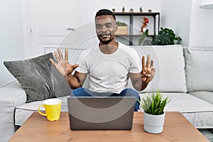 Young african man using laptop at home showing and pointing up with fingers number eight while smiling confident and happy