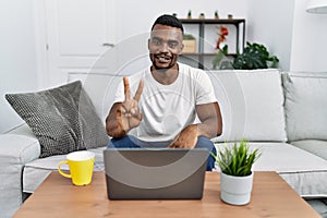 Young african man using laptop at home showing and pointing up with fingers number two while smiling confident and happy