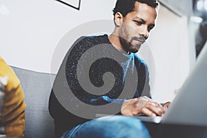 Young African man using laptop while sitting at his modern coworking place.Concept of pensive business people.Brick wall