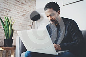 Young African man using laptop while sitting sofa at his modern coworking studio.Concept of full concentration.Blurred