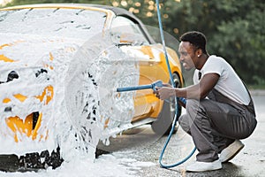 Young African man washing wheels of his luxury car spraying the foam with high pressure .