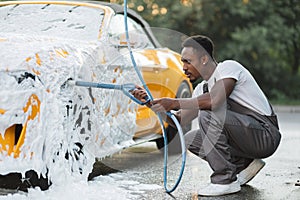 Young African man washing wheels of his luxury car spraying the foam with high pressure .