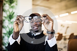 Young african man working at computer holding eyesglasses in front in modern office