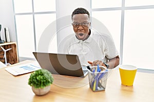 Young african man working at the office using computer laptop afraid and shocked with surprise and amazed expression, fear and