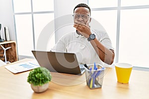 Young african man working at the office using computer laptop bored yawning tired covering mouth with hand