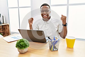 Young african man working at the office using computer laptop celebrating surprised and amazed for success with arms raised and